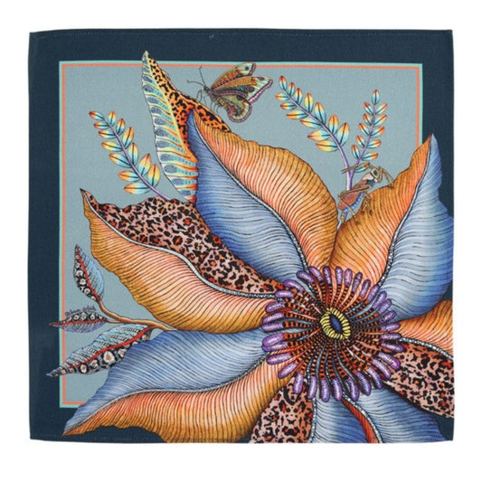 Thanda Bloom napkin in mist blue with a large orange and blue flower, butterfly, foliage, and dark border.