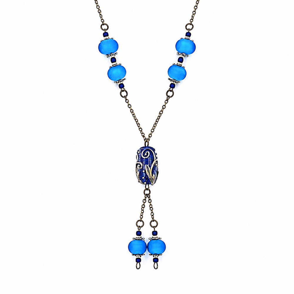 Close-up of a handmade blue lariat necklace showing bright blue glass beads with silver-tone accents, antique-bronze chain, a detailed deep blue focal bead, and matching dangling bead drops.