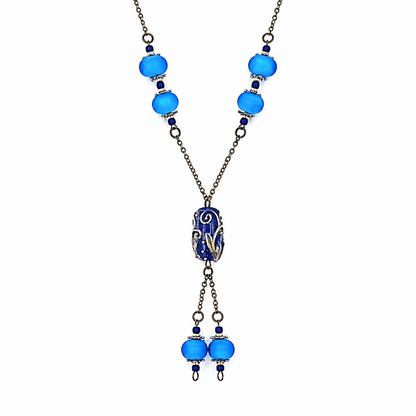 Close-up of a handmade blue lariat necklace showing bright blue glass beads with silver-tone accents, antique-bronze chain, a detailed deep blue focal bead, and matching dangling bead drops.