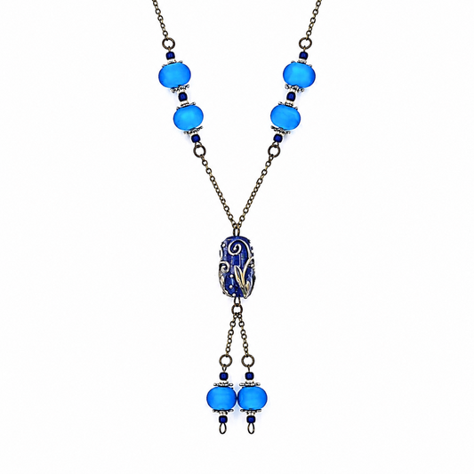 Close-up of a handmade blue lariat necklace showing bright blue glass beads with silver-tone accents, antique-bronze chain, a detailed deep blue focal bead, and matching dangling bead drops.