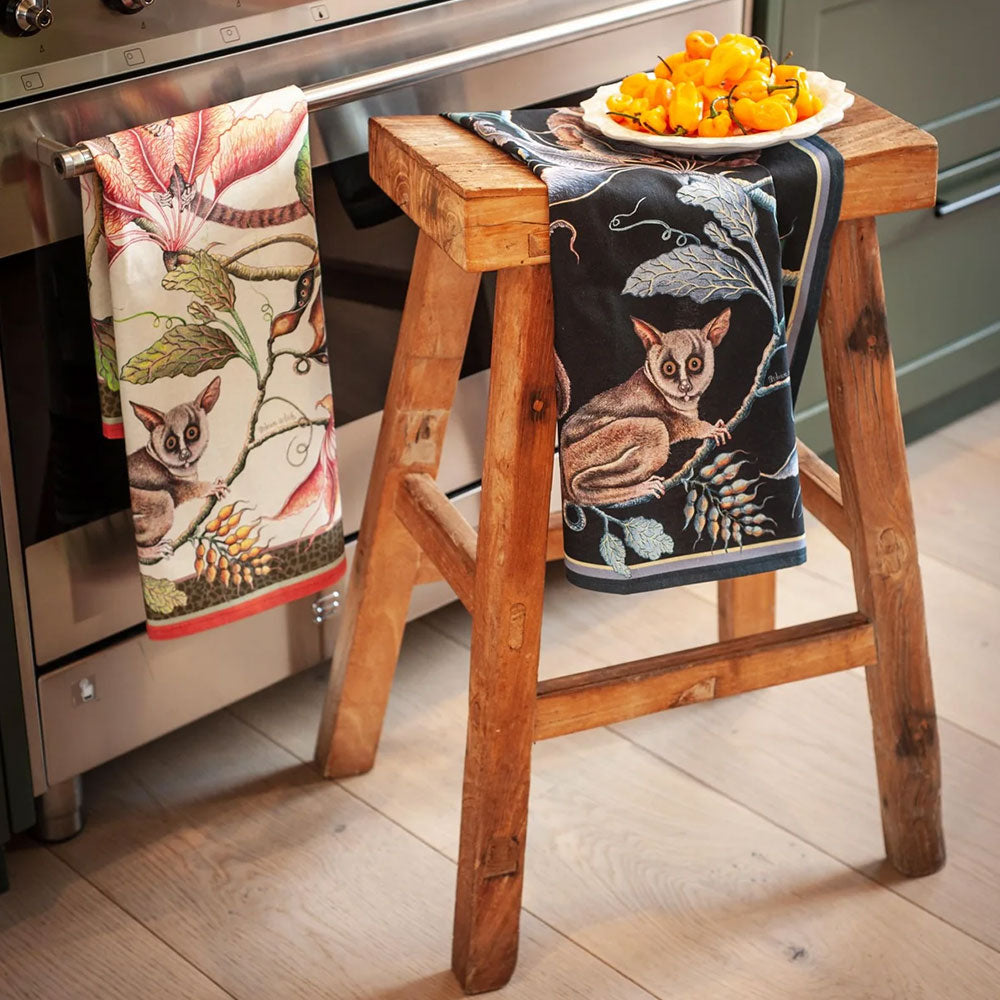Bush Baby Tea Towels styled in a kitchen, with one draped over a wooden stool and another hanging from an oven beside a bowl of bright orange peppers. 