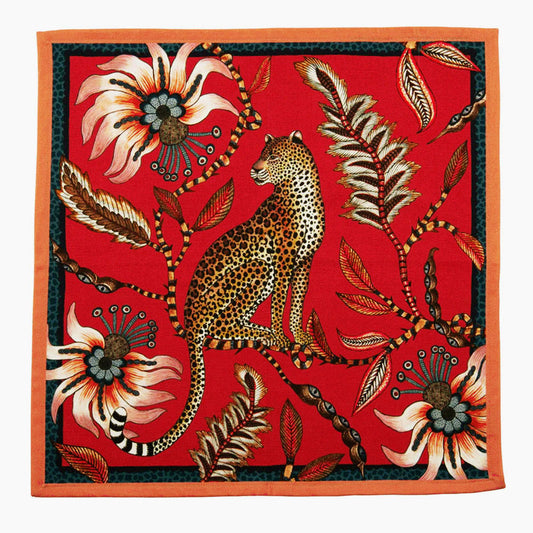 Leopard Napkin by Ardmore featuring a seated leopard surrounded by oversized flowers leaves and botanical details on a vivid red background with a dark green and orange border.