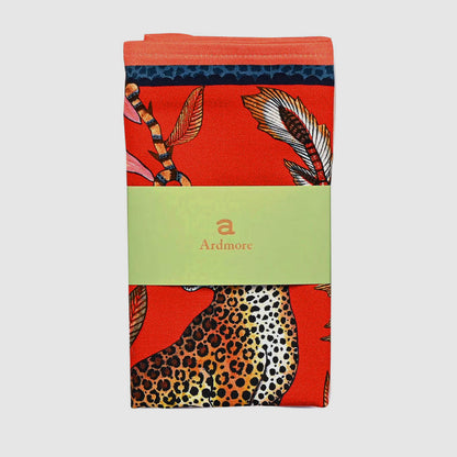 Folded Leopard Napkin by Ardmore wrapped with a light green branded paper band showing sections of the red botanical print and spotted leopard design.