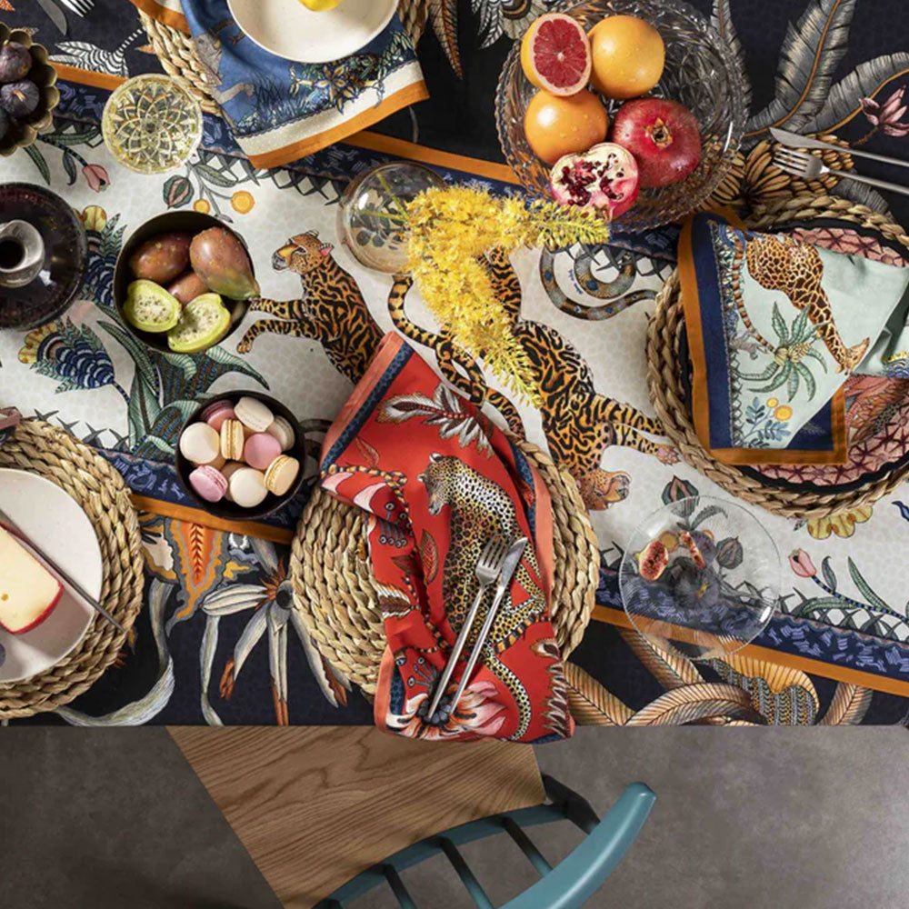 Styled dining table featuring Leopard Napkins by Ardmore among patterned table linens fruit candles glassware woven placemats and decorative tableware.