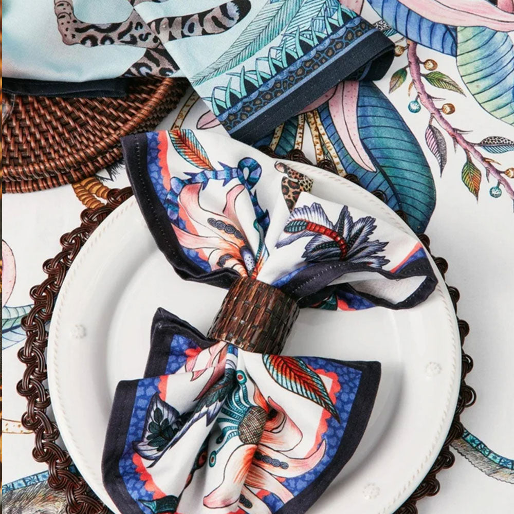 Leopard-and-floral cloth napkin styled with a woven napkin ring on a white place setting alongside coordinating botanical table linens.