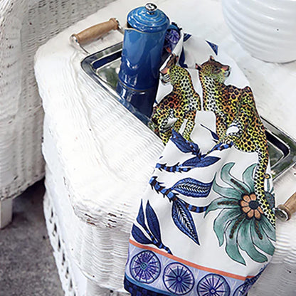 Lovebird Leopards Tea Towel styled over a serving tray beside blue tableware, showing the paired leopard design with blue botanical details and flowers.