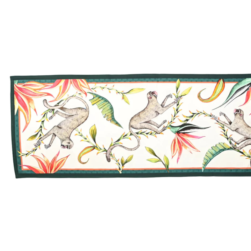 Full view of the Monkey Paradise Table Runner Large featuring illustrated monkeys among tropical leaves and flowers on a cream background with a dark green border