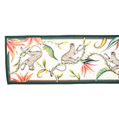 Full view of the Monkey Paradise Table Runner Large featuring illustrated monkeys among tropical leaves and flowers on a cream background with a dark green border