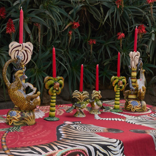 Close-up of an outdoor table setting featuring the red Ardmore wildlife tablecloth, zebra motifs, sculptural candleholders, and red taper candles.
