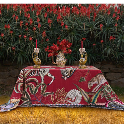 Red Ardmore wildlife tablecloth styled on an outdoor table with decorative animal candleholders, red candles, flowers, and coordinating textiles.