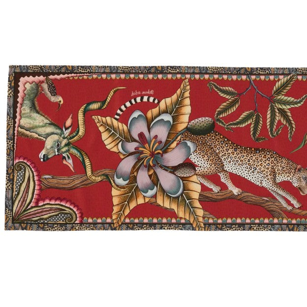 Close-up of the Ardmore table runner showing antelope, a spotted big cat, an oversized flower, and leafy branches against a red background.