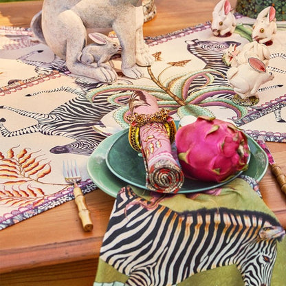 Ardmore wildlife table runner styled on a wooden dining table with zebra-print linens, decorative rabbit figurines, green dinnerware, and botanical accents.