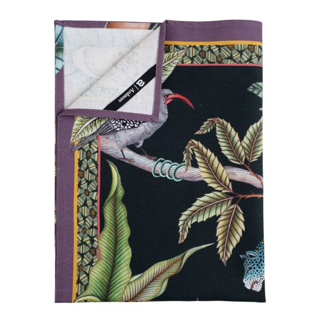 Folded Ardmore tea towel showing a bird, leafy branches, tropical plants, and a purple patterned border with the brand label visible.
