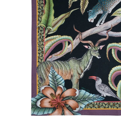 Close-up of the Ardmore tea towel featuring a kudu antelope, spotted bird, flowering plant, tropical leaves, and part of a leopard against a black background with a purple border.
