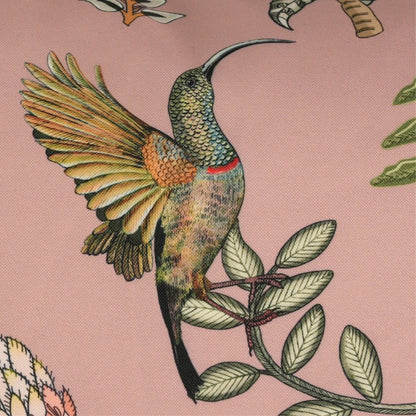 Close-up of a colorful hummingbird with outstretched wings perched among green leaves on a blush pink background.