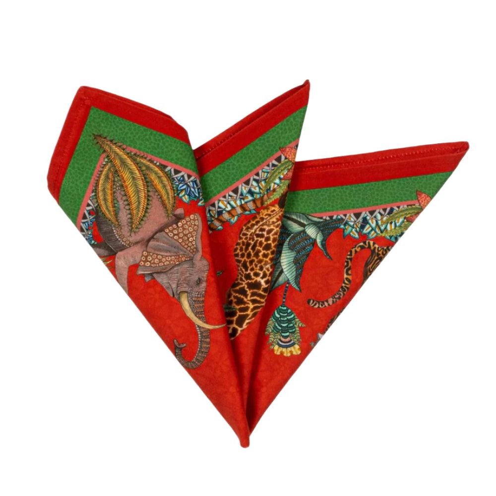 Sabie Forest Napkin folded into a decorative fan shape, showing illustrated elephant, giraffe, tiger, tropical leaves, and green border details on a vivid red background.