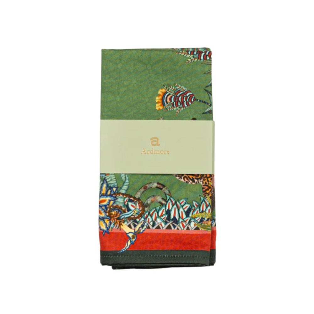 Folded Sabie Forest Napkin by Ardmore wrapped with a light green branded paper band, showing sections of the green wildlife and botanical print with red and dark green borders.