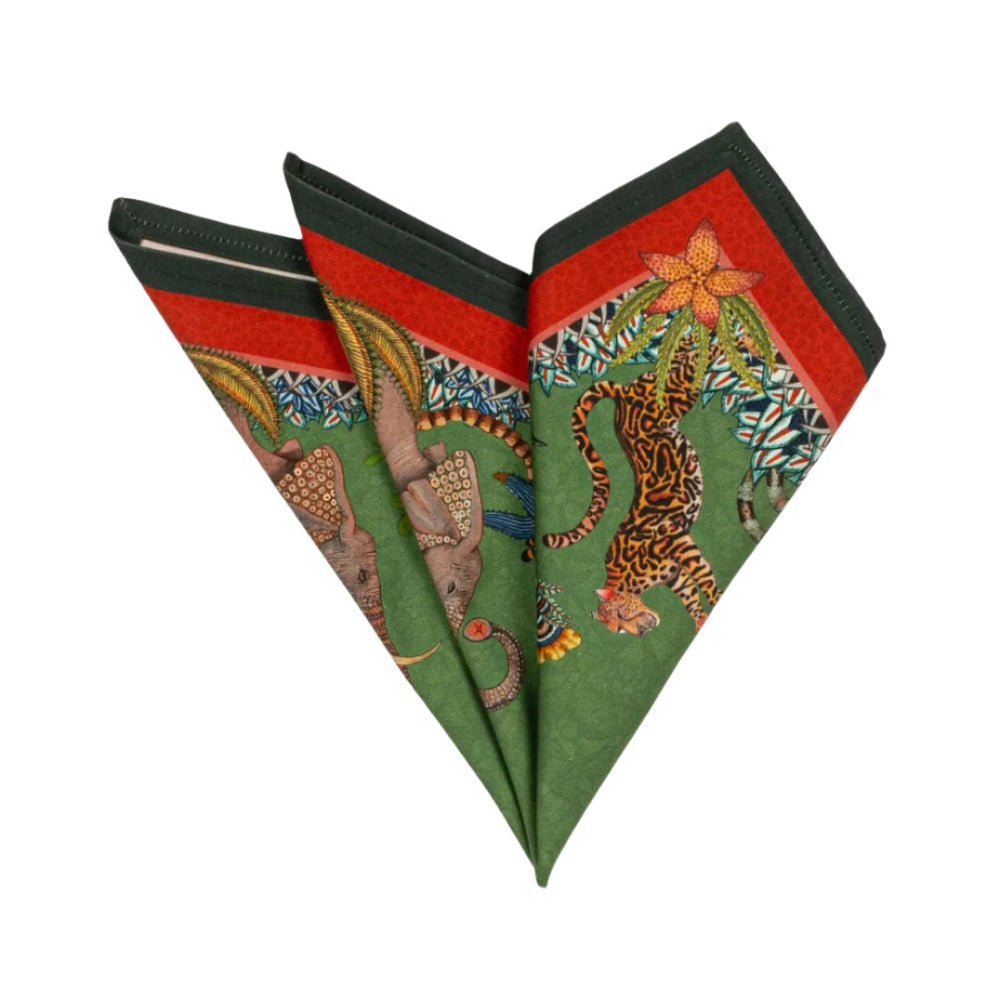 Sabie Forest Napkin folded into a decorative fan shape, showing illustrated elephants, tiger, tropical foliage, and red and dark green border details on a green background.