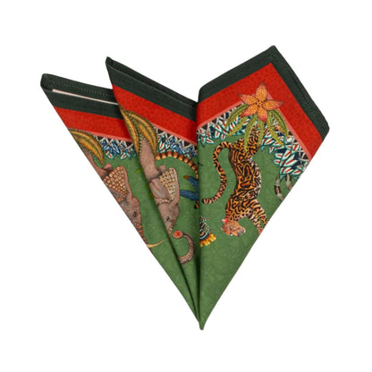 Sabie Forest Napkin folded into a decorative fan shape, showing illustrated elephants, tiger, tropical foliage, and red and dark green border details on a green background.