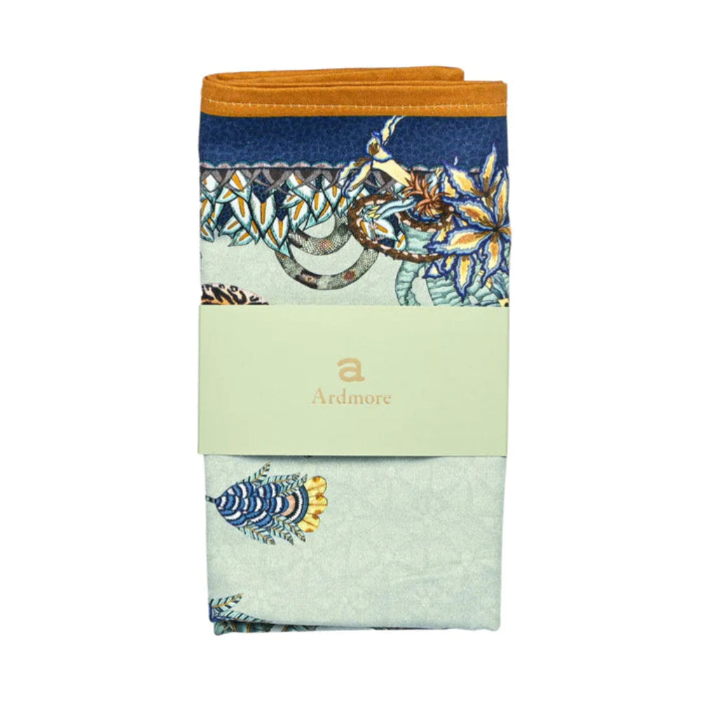 Folded Sabie Forest Napkin by Ardmore wrapped with a light green branded paper band, showing sections of the pale aqua wildlife print with navy and ochre border details.