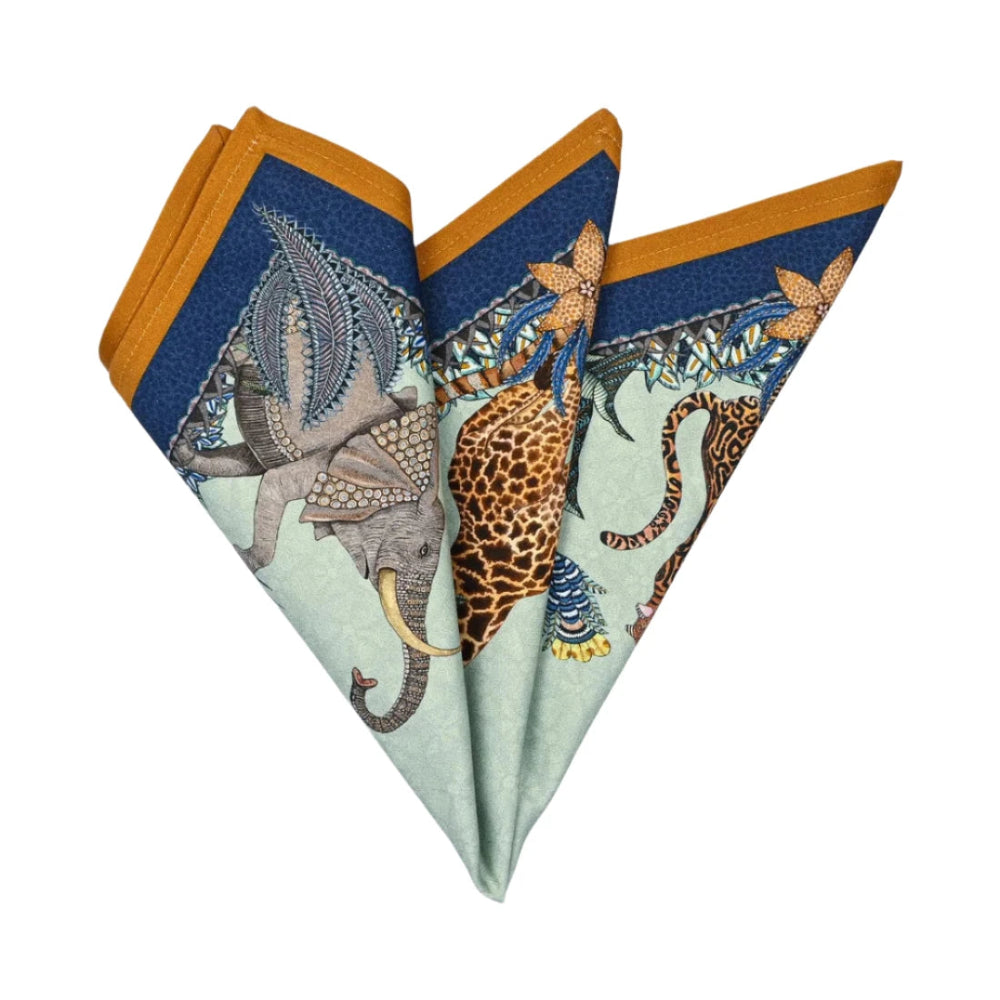 Sabie Forest Napkin folded into a decorative fan shape, showing illustrated elephants, giraffe, tiger, tropical foliage, and deep navy and ochre border accents.
