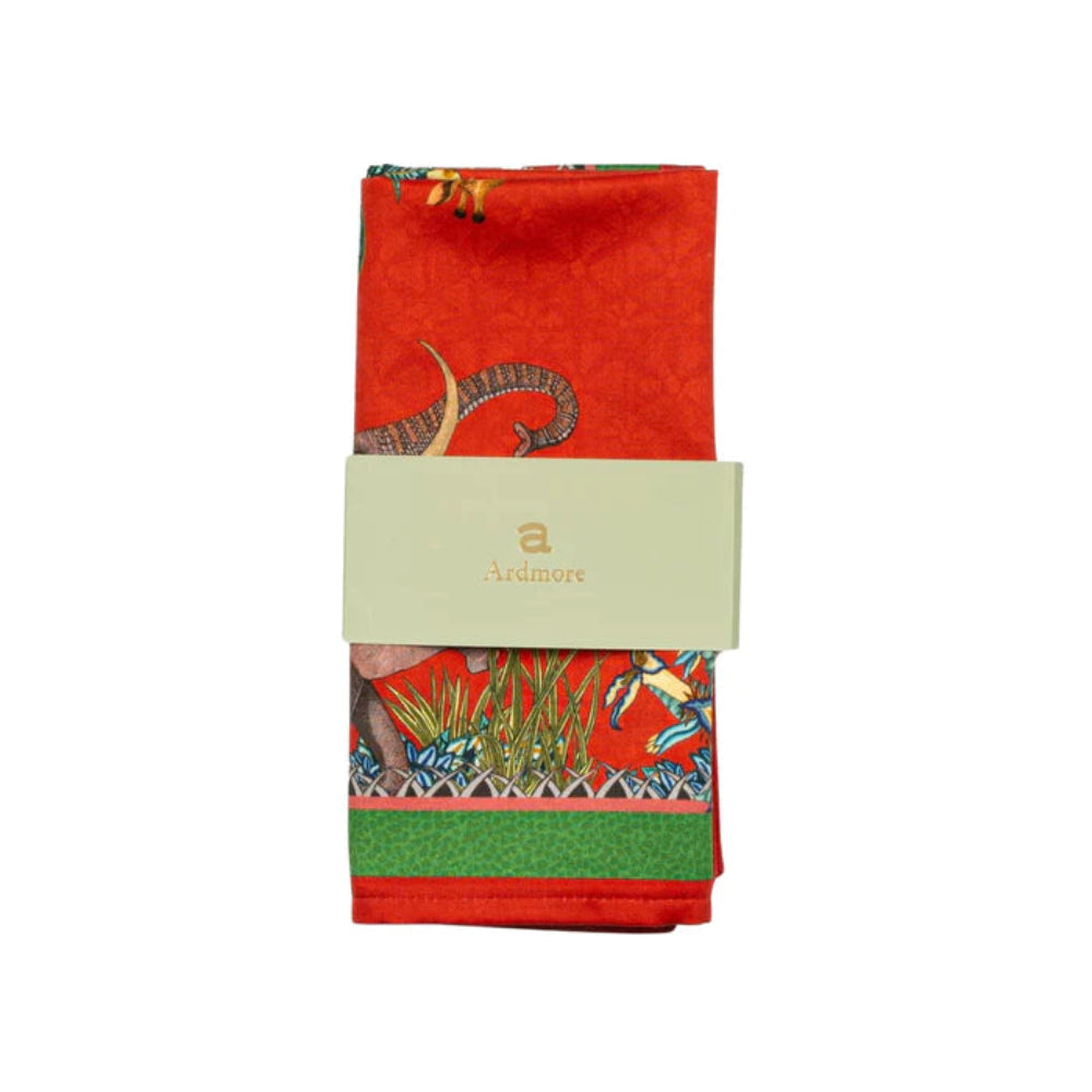 Folded Sabie Forest Napkin by Ardmore wrapped with a light green branded paper band, showing portions of the red wildlife and botanical print with a green border.