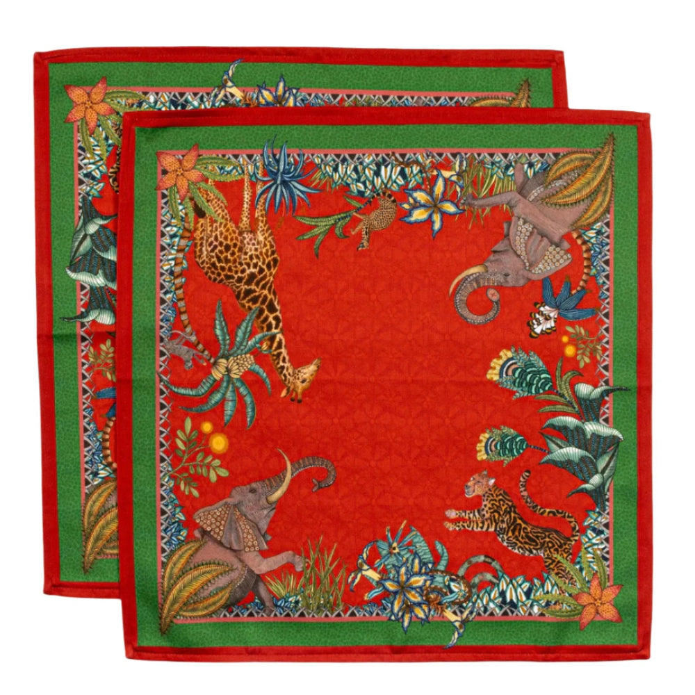 Two Sabie Forest Napkins layered together, featuring a red background with green borders and illustrated giraffe, elephants, tiger, flowers, and tropical foliage.