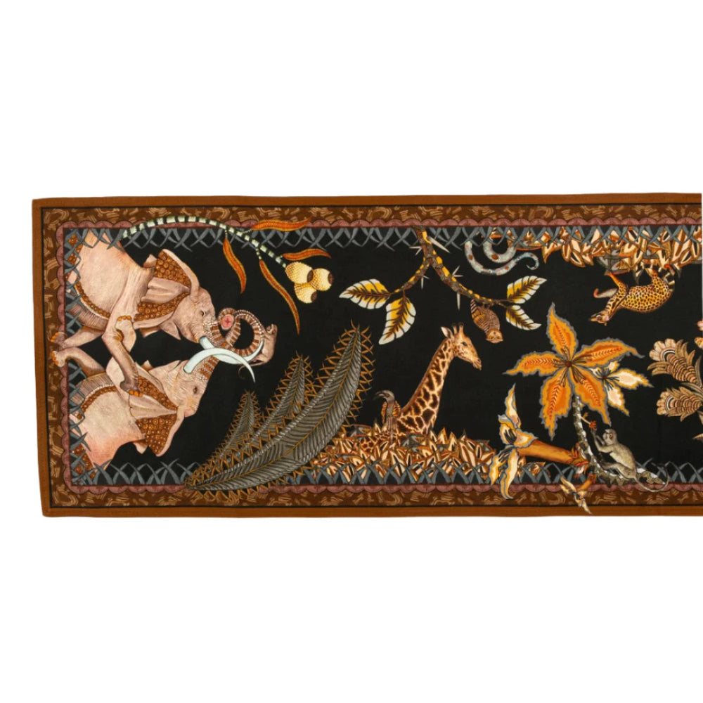 Full horizontal view of the Sabie Forest Table Runner Small in black laid flat, showcasing an intricate safari scene on a black background with elephants, a giraffe, a monkey in a palm tree, and lush flora framed by a brown border.