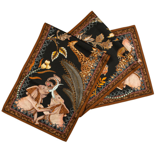 The Sabie Forest Table Runner Large in black folded into overlapping layers, featuring a dark background detailed with safari wildlife illustrations including elephants and a giraffe, framed by a brown patterned border.