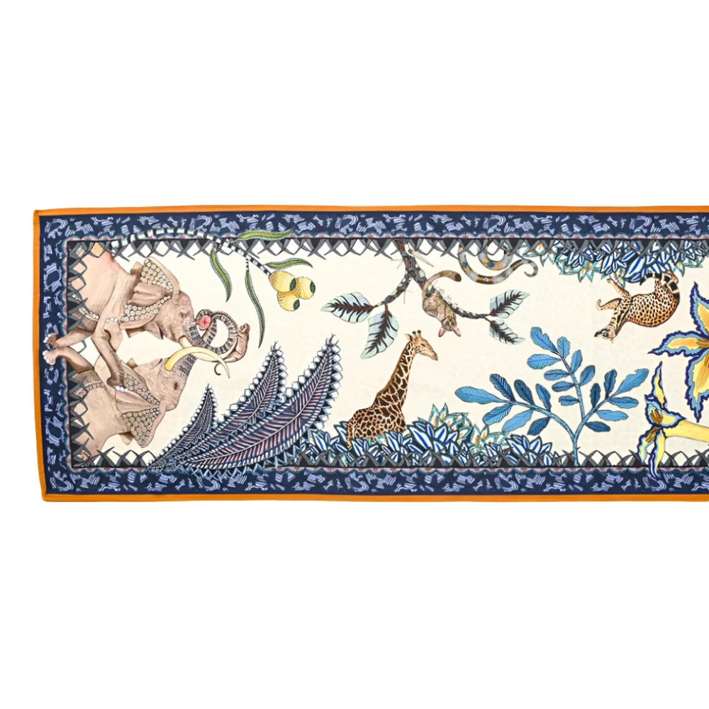 A full horizontal view of the Sabie Forest Table Runner Small laid flat, featuring an off-white center illustrated with elephants, a giraffe, leopards, and botanical flora, enclosed by a blue patterned border and gold rim.
