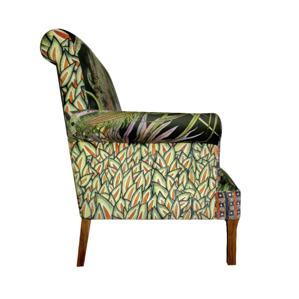 Side profile view of the Sabie Sofa displaying the outer side panel covered in a dense green leafy pattern and dark wooden legs.