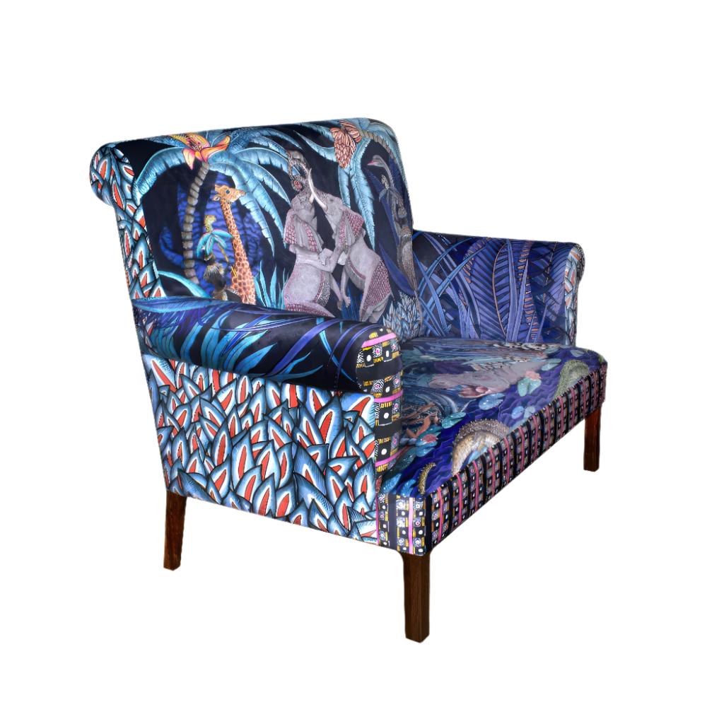 Three-quarter view of the Sabie Sofa showcasing its rolled arms, blue jungle-themed safari upholstery, geometric side print, and dark wooden legs.