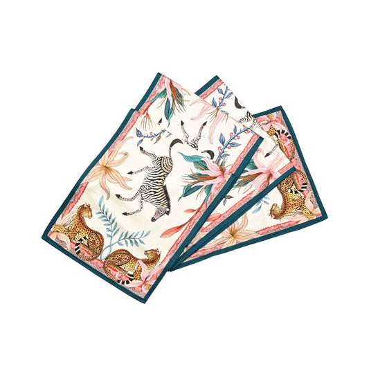 The Sabie Forest Table Runner Small folded in overlapping layers, displaying a light cream background illustrated with a leaping zebra, leopards, tropical flora, and a dark teal border.