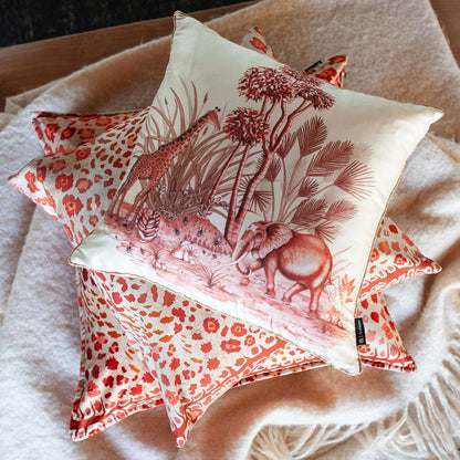 The rust-red leopard spot Safari Pillow stacked underneath a matching cream pillow featuring an illustrated safari scene with a giraffe and elephant.