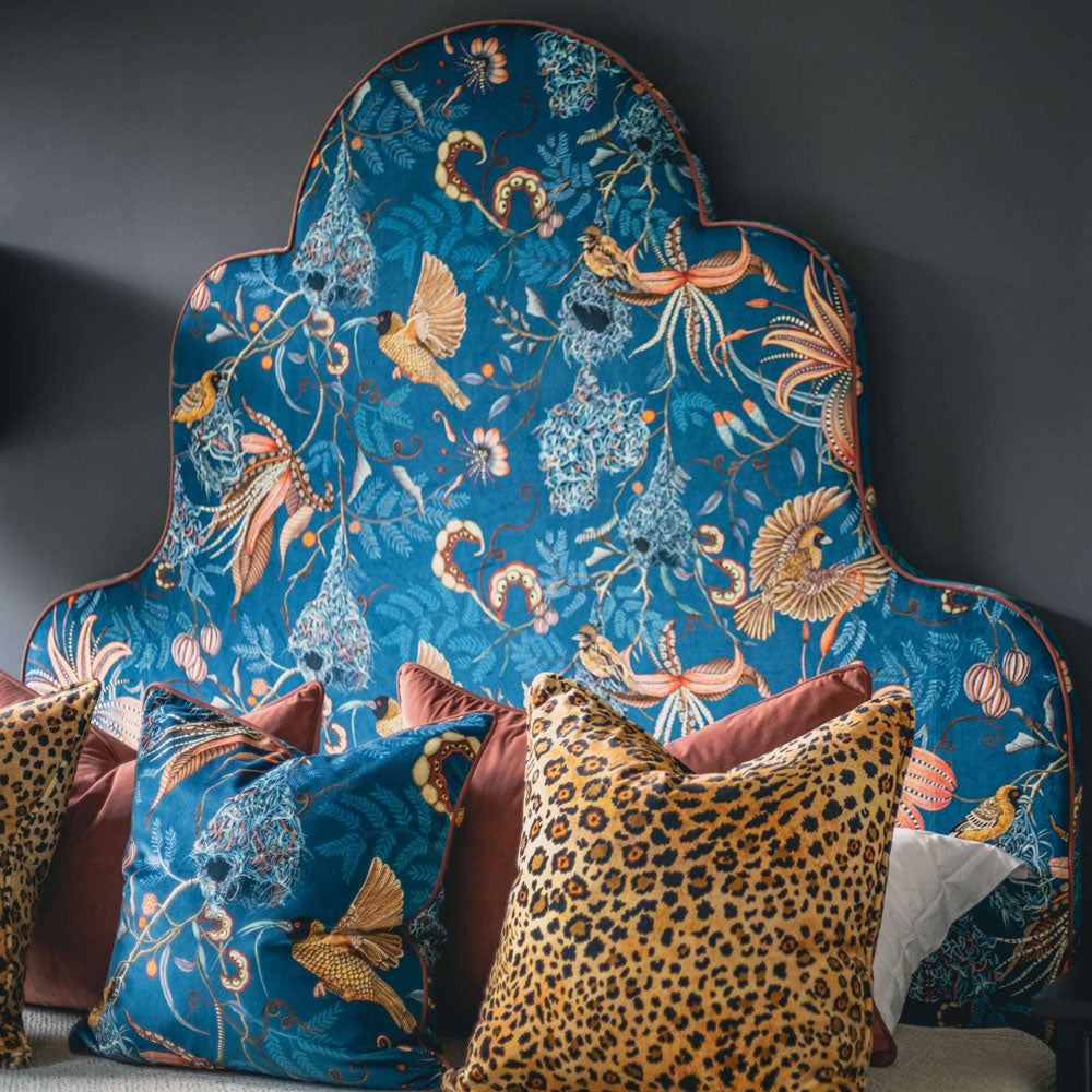 The Safari Spot Pillow styled on a bed alongside blue floral and terracotta pillows against a decorative blue botanical headboard.
