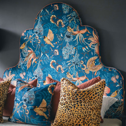The Safari Spot Pillow styled on a bed alongside blue floral and terracotta pillows against a decorative blue botanical headboard.