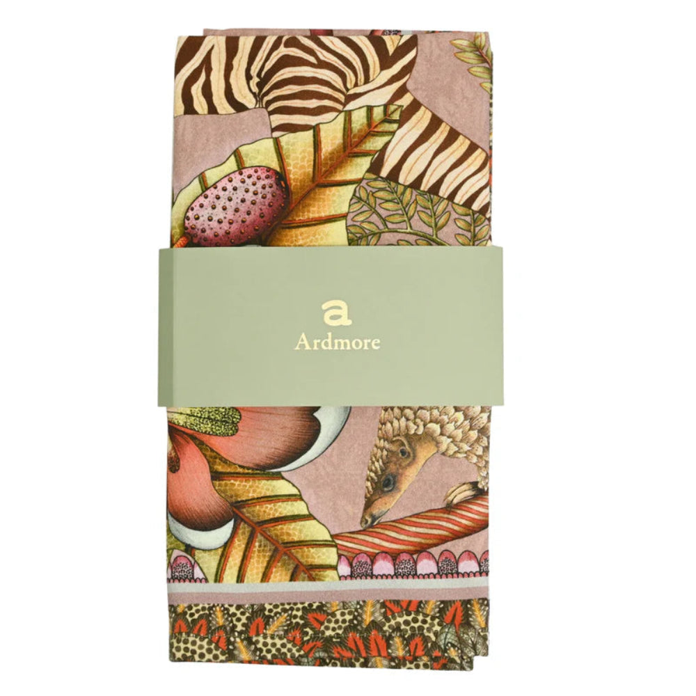 Folded Thanda Stripe Napkin by Ardmore wrapped with a light green branded paper band, showing sections of the zebra print, tropical leaves, flowers, and decorative border.