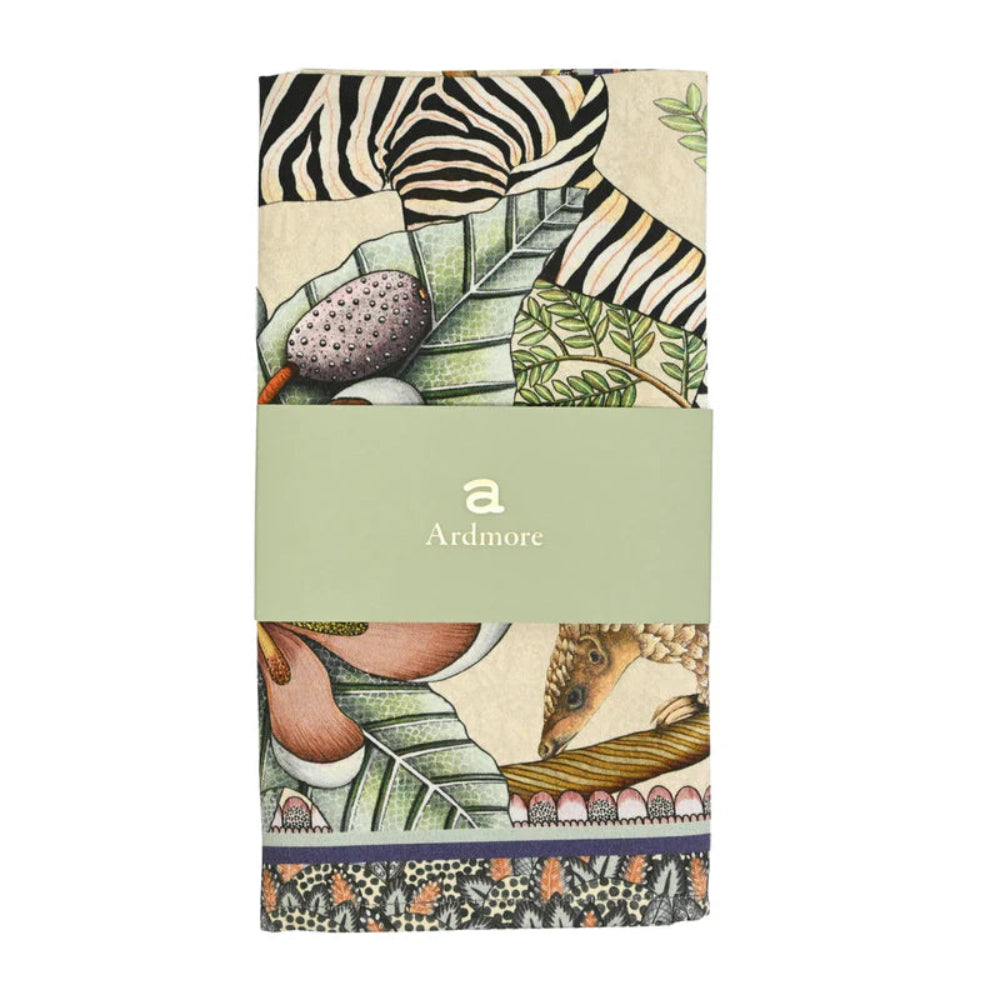 Folded Thanda Stripe Napkin by Ardmore wrapped with a light green branded paper band, showing portions of the zebra stripe pattern, tropical foliage, and botanical artwork.