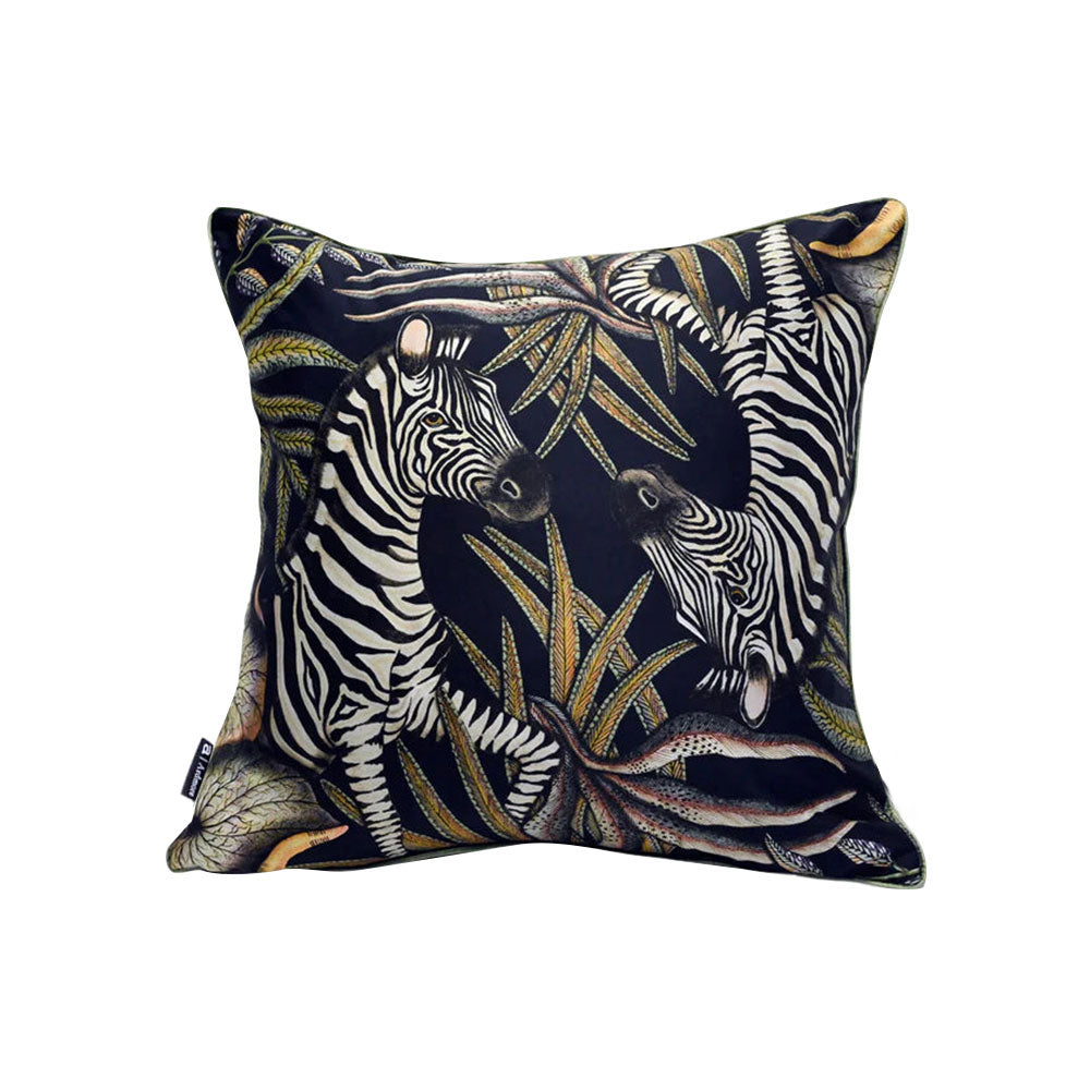 Thanda Stripe Pillow shown from a slightly different angle, featuring a pair of zebras among detailed tropical leaves in cream, olive, gold, and earthy tones on a black background.