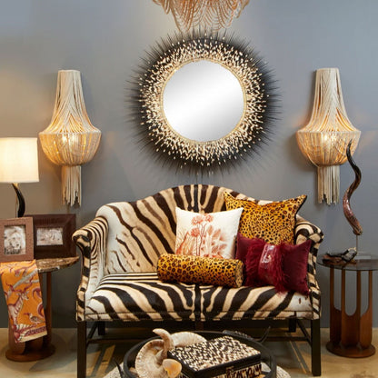 The white and blue Thanda Toile Pillow styled indoors on a grey armchair alongside decorative patterned cushions.
