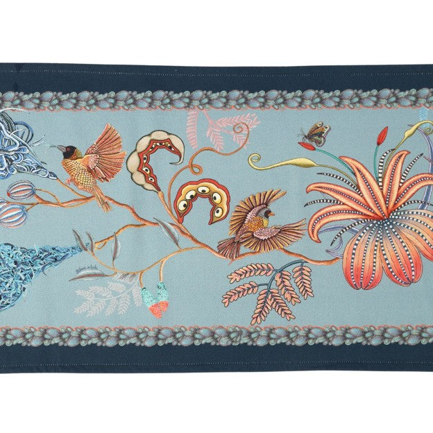 Close-up of the Ardmore table runner showing two illustrated birds, oversized flowers, seedpods, vines, and a richly patterned blue border.