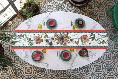 Ardmore bird-and-botanical table runner styled across a white oval dining table with colorful place settings and glassware.