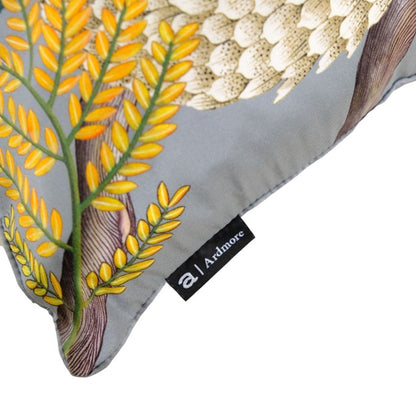 Three Ardmore pangolin-print decorative pillows in gray, dark charcoal, and cream displayed outdoors against dried grass.
