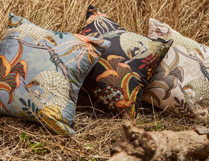 Three Ardmore pangolin-print decorative pillows in gray, dark charcoal, and cream displayed outdoors against dried grass.