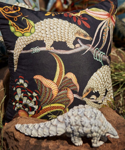 Black Ardmore pangolin-print decorative pillow displayed outdoors behind a sculpted pangolin figurine.